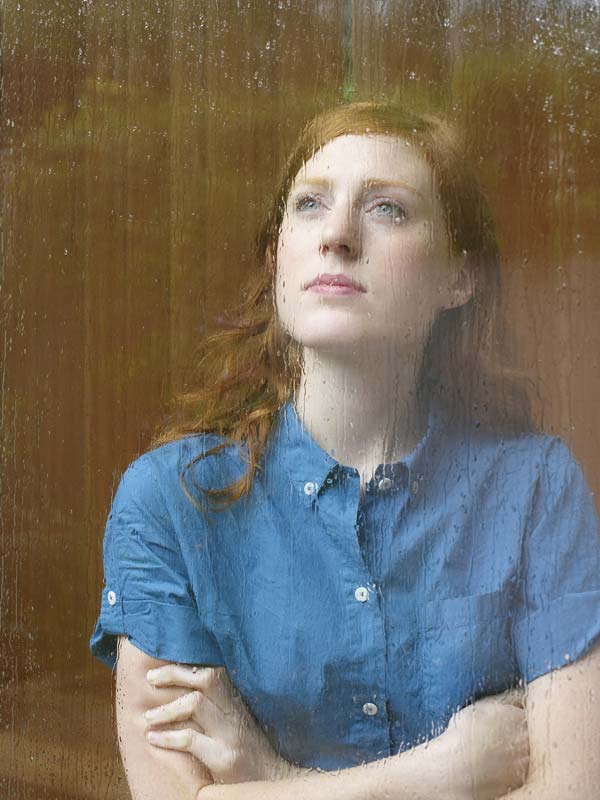 Red haired woman looking longingly out window with rain, dealing with persistent depression.